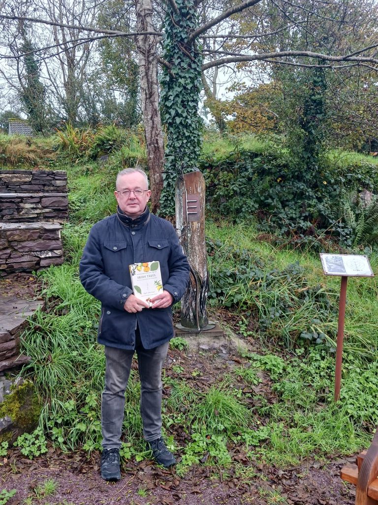 Author Niall Mac Coitr pictured beside the alder sculpture in the Wild Garden